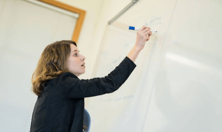 A professor writes on a whiteboard with a blue expo marker.