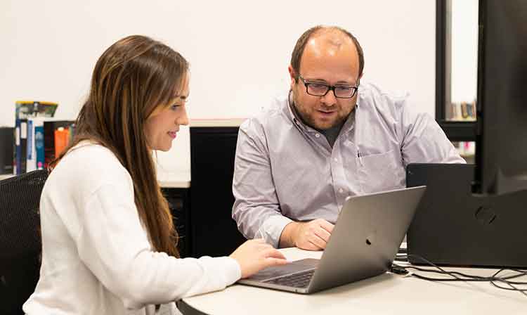 Two people sit in front of an open laptop.