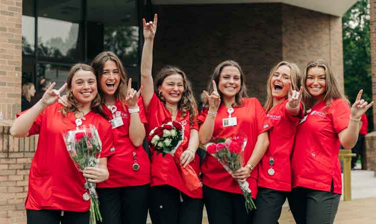 A group of people in red scrubs smile and hold up their hands.