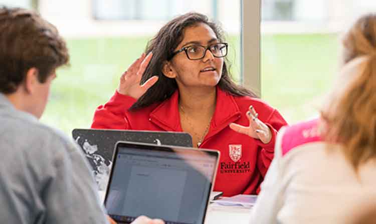 A woman in a red jacket raising her hand in class.