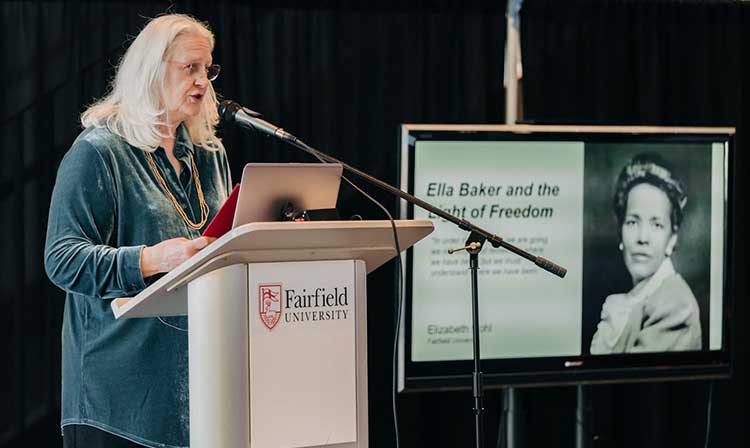 A Black Studies professor giving a presentation on MLK day with a screen in the back showing a picture of Ella Baker that reads “Ella Baker and the Fight of Freedom” 