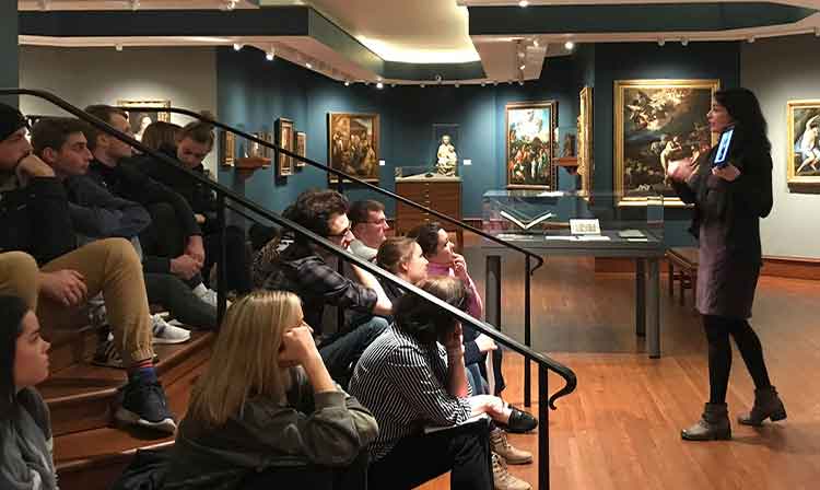 Art History students sitting down listening to a presentation in an art history museum. 