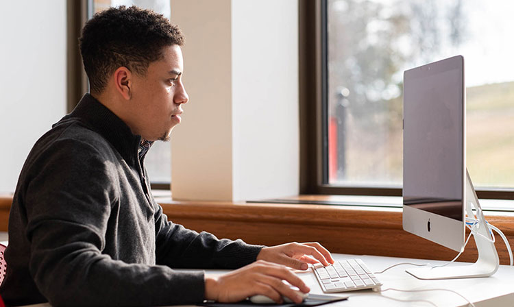 A student is sitting at a computer looking at the screen intently. 