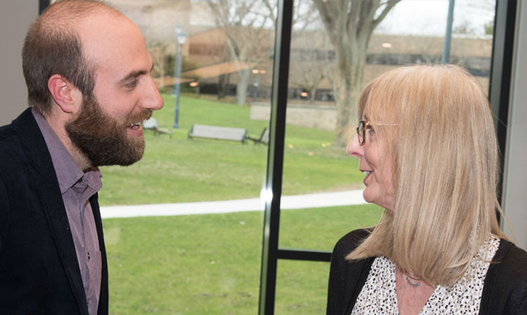 Two faculty members smiling and facing each other talking. 