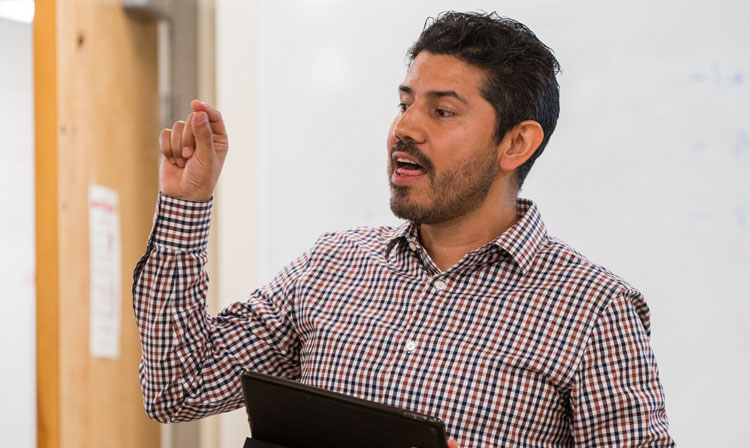 Professor speaking to class with tablet in his hand.