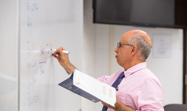 Side profile of an engineering professor writing equations on a white board. 