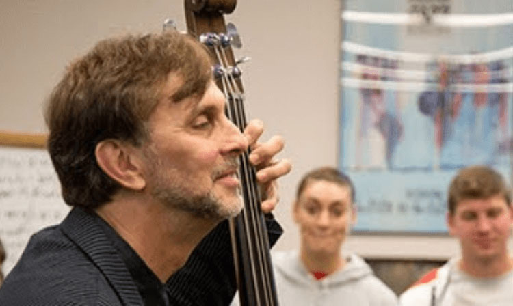 Music professor sitting and smiling playing the standing bass guitar. 