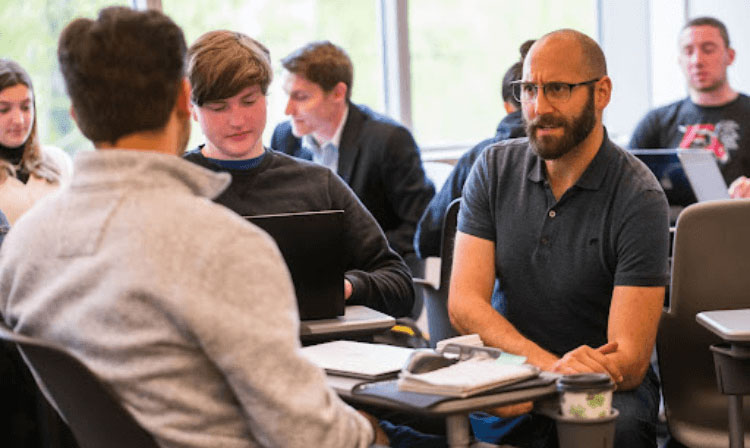 Students and professors sit across from one another talking in a crowded classroom. 