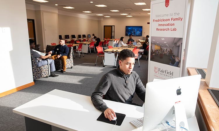 A student sits at a desk and uses an Apple Desktop computer.