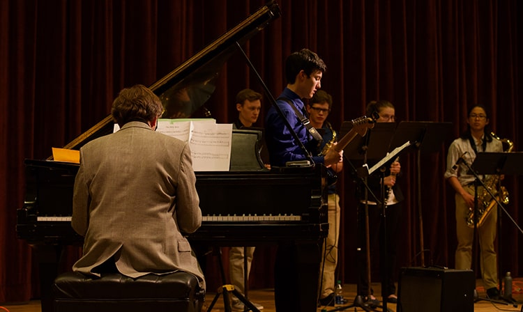 Students playing various instruments in front of their professor who is playing piano.