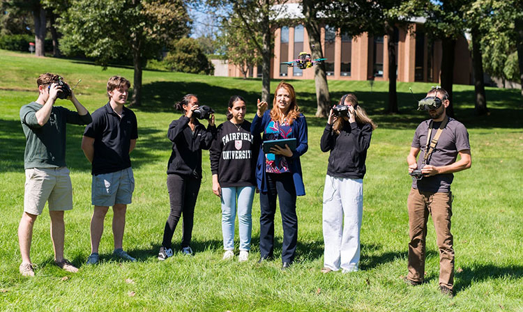 Students gather in a field, using a drone, surrounded by nature.