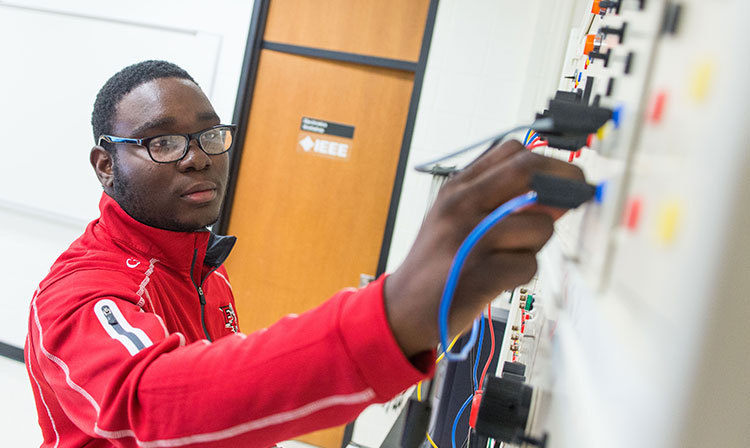 Side profile of a student plugging something into a wall of cables. 