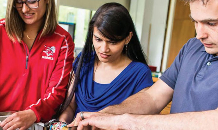 In a lab, three individuals work together on a project, focused on their tasks and using various tools.