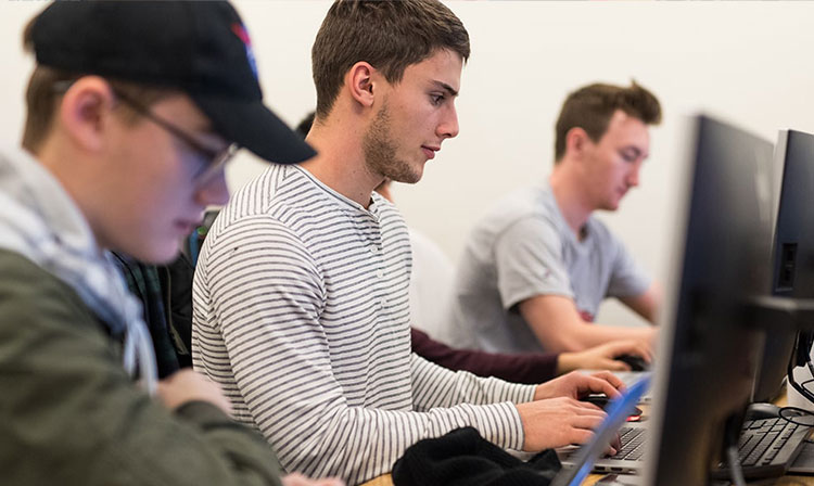 Students focused on computers, collaborating and learning in a bright classroom setting.