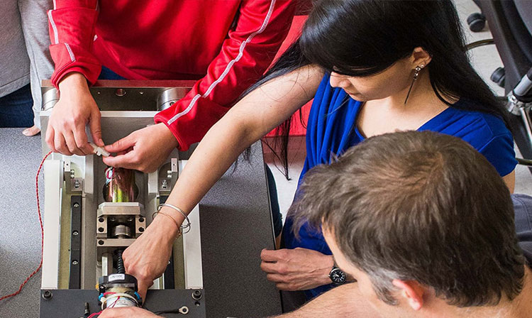 A diverse group of people collaborating on a large machine in a workshop setting.