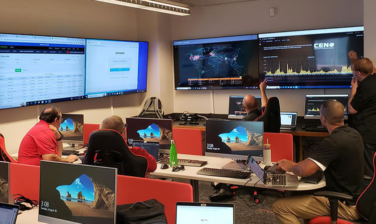 A group of people gathered in a large room, focused on multiple monitors displaying various information.