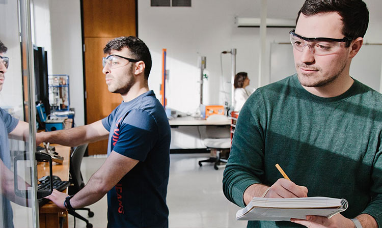 Two men wearing glasses collaborate at a desk in a lab. 