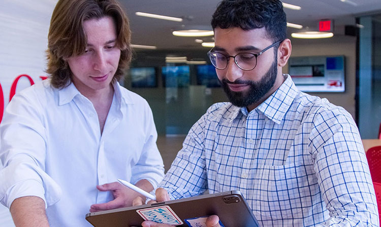 Two men in white shirts focused on a tablet, sharing ideas and discussing what they see.