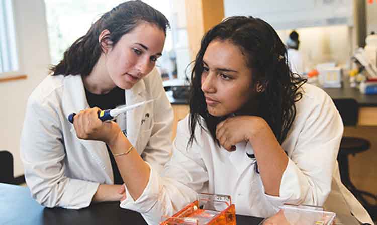 2 students working in a science lab wearing white coats.