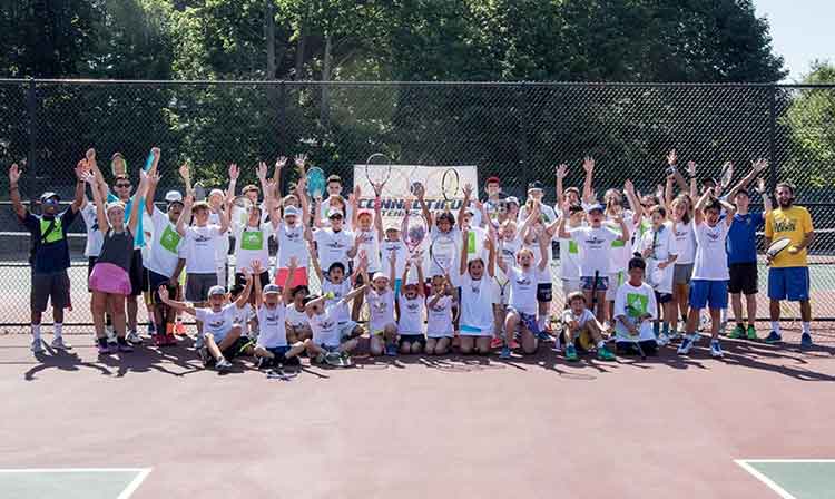 CT tennis camp takes a group photo with arms raised on the court 