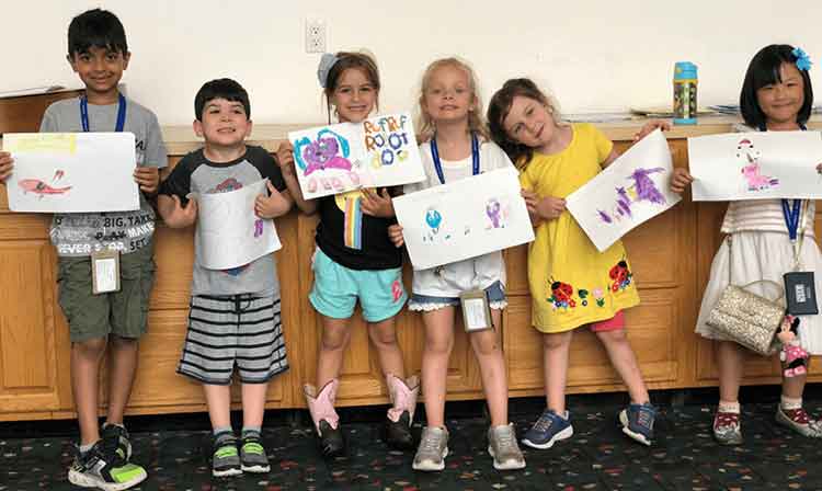 6 young students hold up their drawings and smile 