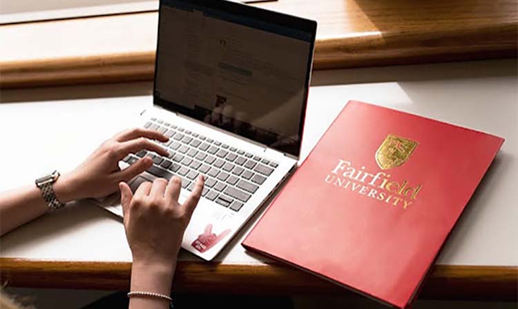 Closeup of a laptop and red Fairfield University booklet. 