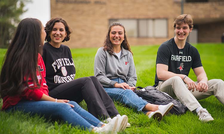 Students sitting on a grassy hill on campus laughing and talking. 