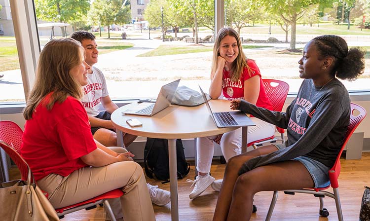 Four students sitting in a collaborative space on campus and talking. 