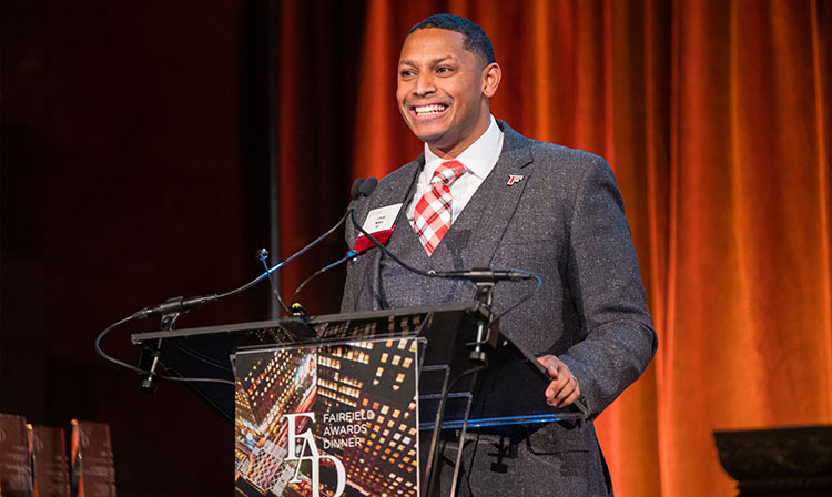 A man in a suit and tie stands confidently at a podium, ready to speak to an audience.