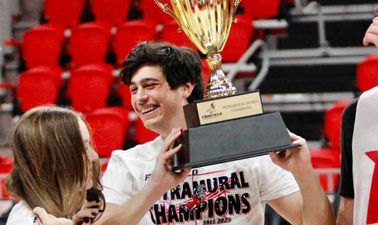 A man proudly holds a trophy, flanked by two smiling women celebrating his achievement.