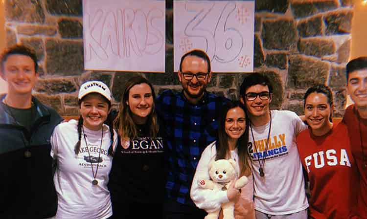 A group of students smile in front of a sign that reads “Kairos 36”. 