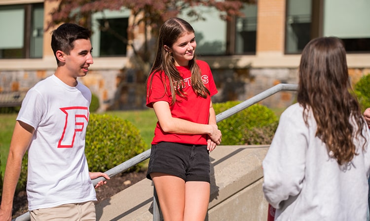 Students stand outside on a set of stairs.