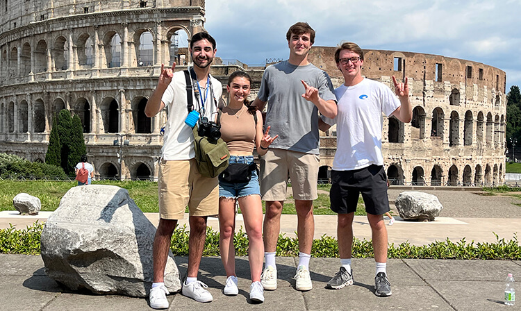 Four students stand in front of the Roman Colosseum.