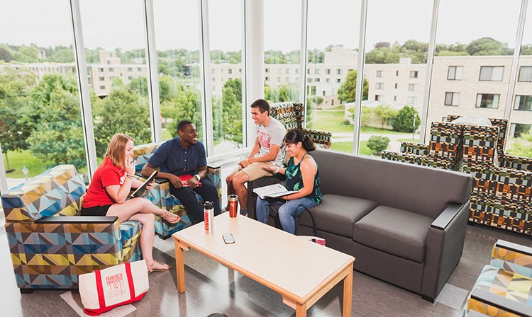 A group of students studying in a well-furnished common room flanked with floor-to-ceiling windows.