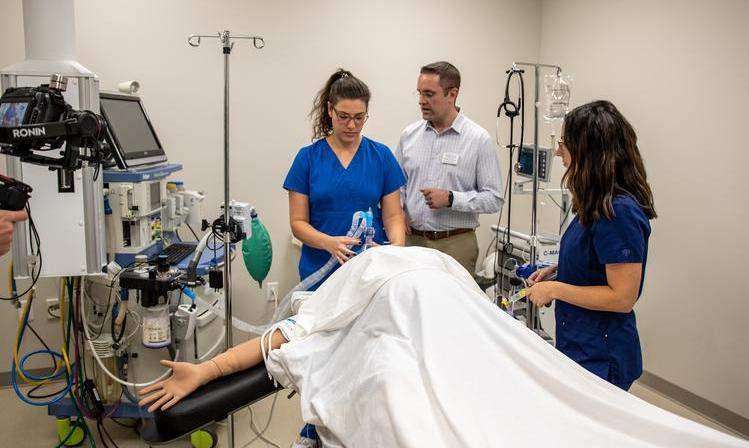 A student learns on a practice dummy while another student observes