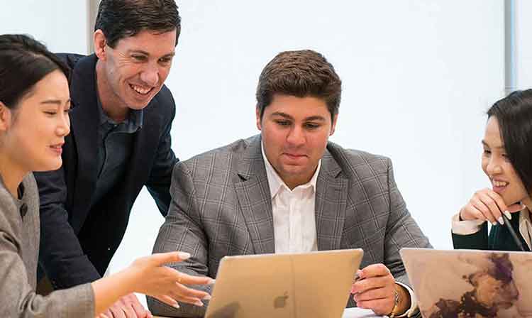 A group of four students sit in front of two open laptops.