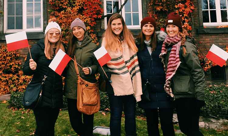 A group of students stand outside of a stone building.