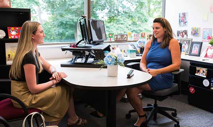 Two people sit at a round table in an office.