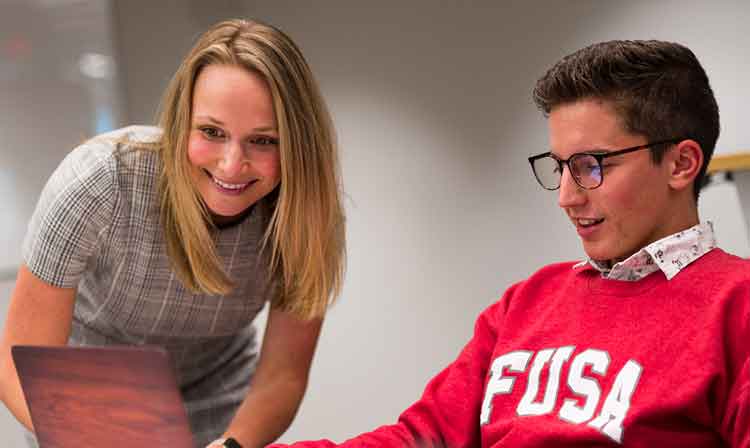 A faculty member speakers speaks with a student wearing a red Fairfield University Student Association sweatshirt.