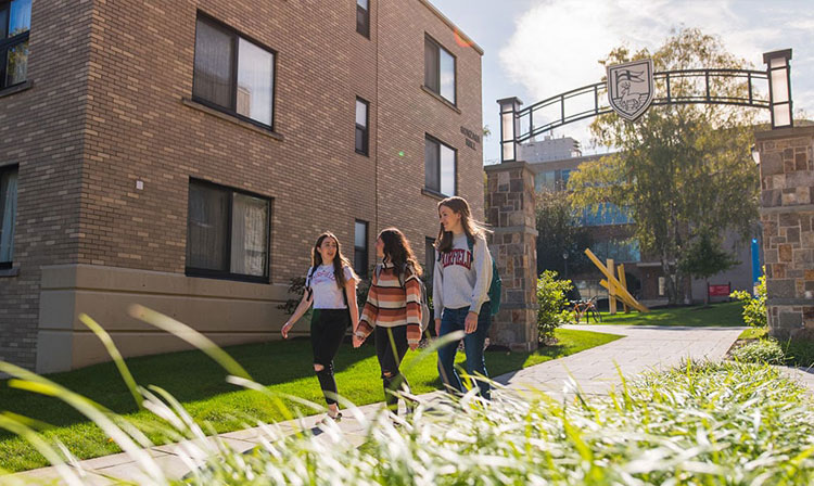 Three students walk outdoors next to a brick building.