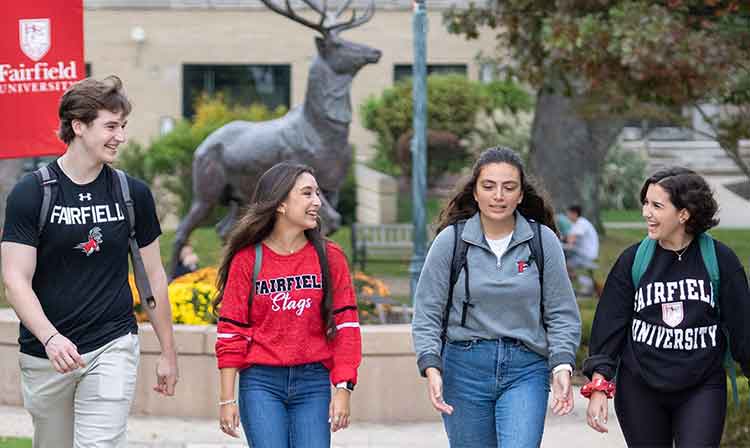 Students walk outdoors past a Stag statue.