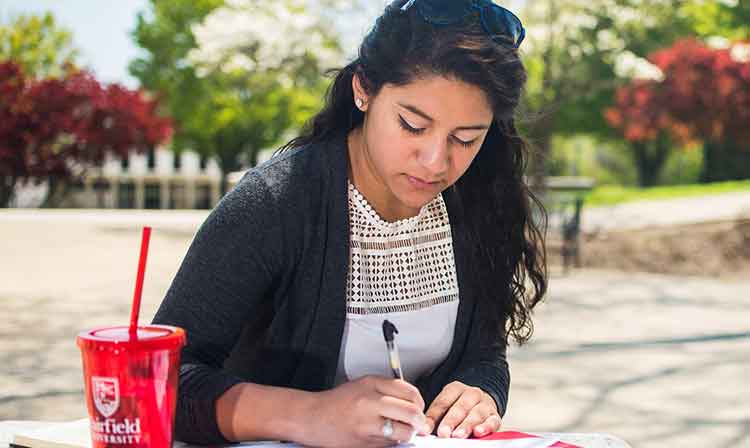 Student taking notes outside at a table.