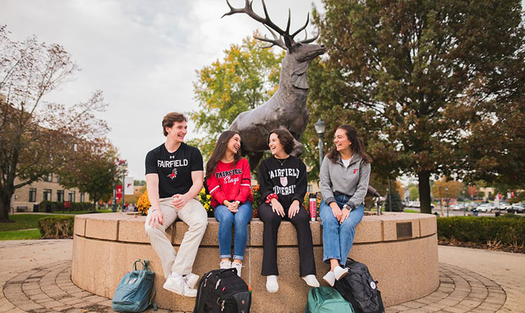 Students sitting and talking in front of the stag statue on campus.