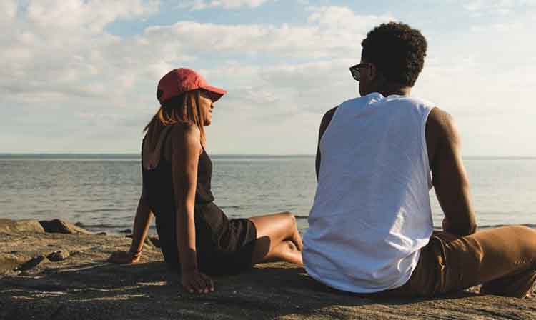 Two students sit on rocks facing a body of water at low tide.