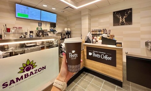 A person holds up a drink from Peet’s Coffee indoors.