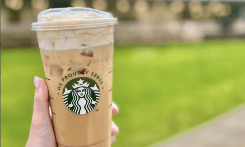 A person holds a Starbucks drink outdoors.