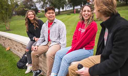 Four students sit on a brick bench outdoors.