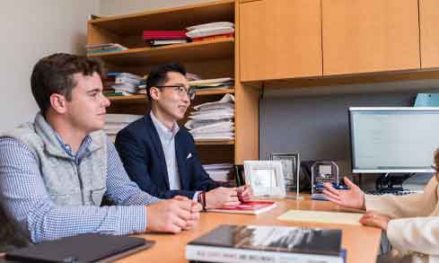 Two students speaking with a professor in an office.