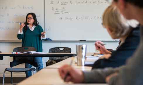 Two students take notes and listen to a lecture from their professor