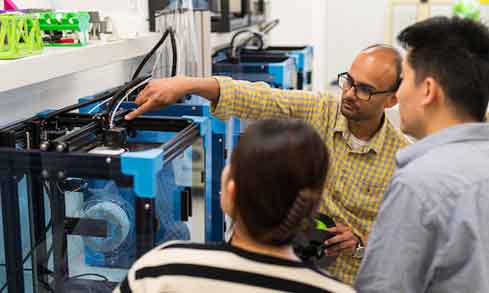 two engineering students watch their professor work on a project